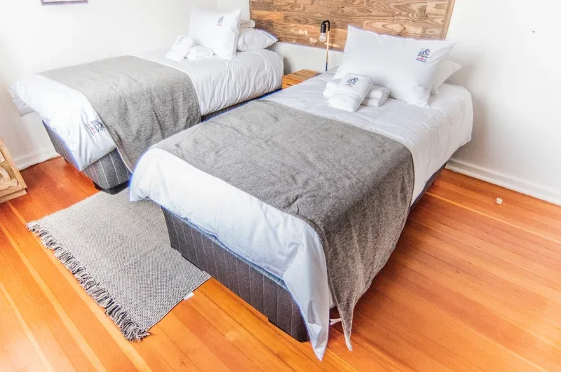 Un dormitorio con dos camas, ropa de cama blanca y mantas grises.