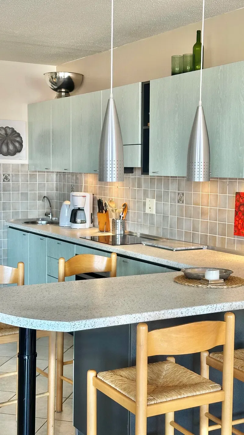 A kitchen with pale blue cabinets, tiled backsplash, and a dining table with chairs.