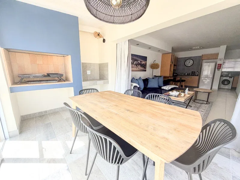 Un comedor con una mesa larga de madera y sillas oscuras da a una sala de estar.