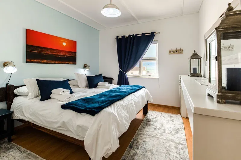 Un dormitorio con ropa de cama blanca, detalles azul oscuro y una imagen de un atardecer sobre la cama.