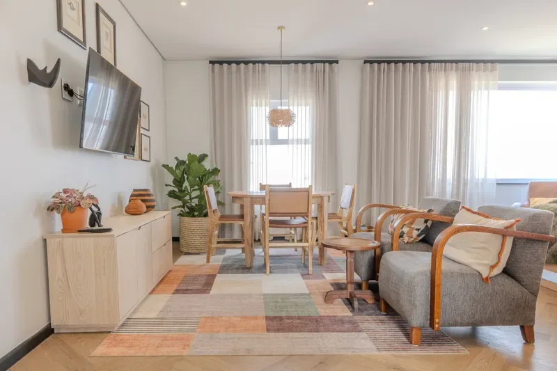 A bright living and dining area with seating, a dining table, and large windows.