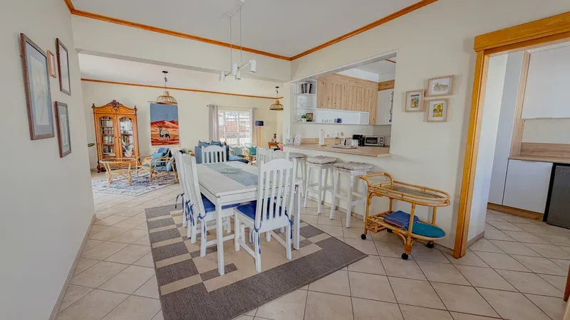 Una zona abierta de comedor y cocina con una mesa larga y sillas blancas.