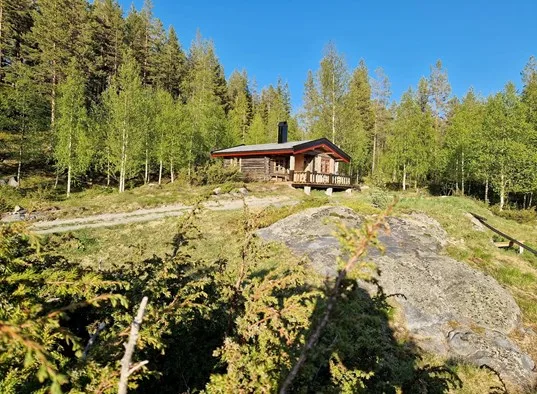 A cabin sits among trees on a rocky, sunlit hillside.