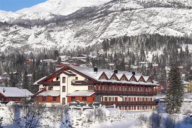 Un gran edificio de estilo alpino se encuentra bajo una ladera montañosa nevada.