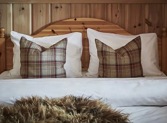 A neatly made bed with plaid pillows rests against a wooden headboard.