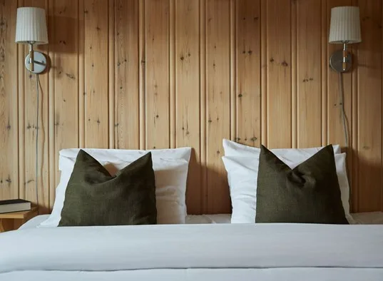 Un dormitorio con dos camas vestidas con ropa blanca frente a una pared revestida de madera.