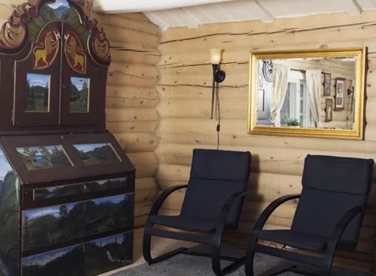 A log-paneled sitting area has two dark chairs beside a decorative display cabinet.