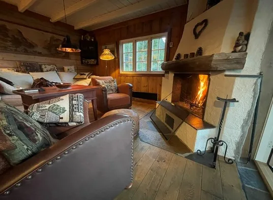 A rustic living room with seating arranged around a lit fireplace.