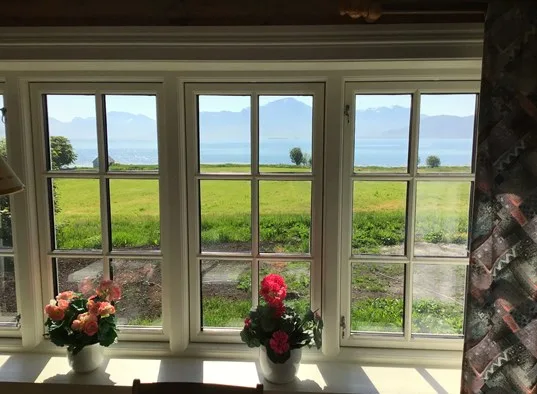 A row of windows overlooks green fields and a distant body of water.