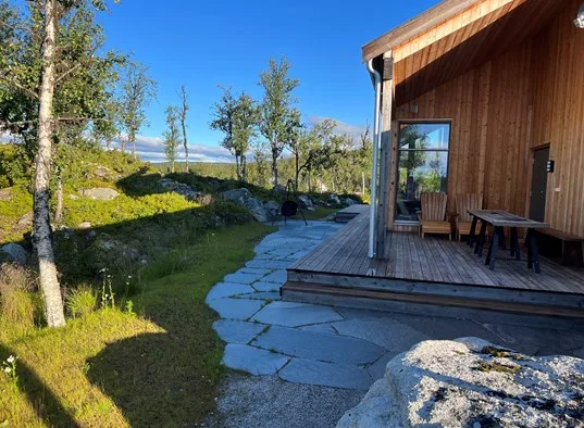 A wooden cabin patio with outdoor seating beside a stone path.