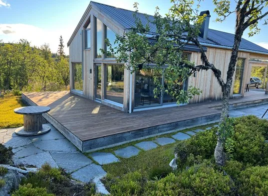 A modern cabin with large windows opens onto a raised wooden deck.
