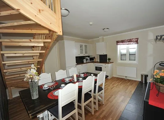 A dining area beneath a wooden staircase opens onto a compact kitchen.