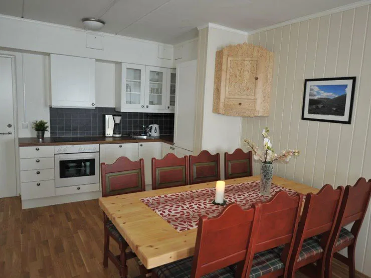 A dining area with a wooden table and red chairs beside a kitchen.