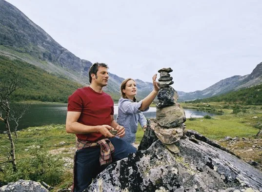 Una pareja construye un pequeño montón de piedras junto a un lago de montaña.