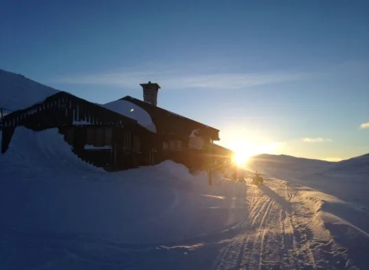 A snow-covered mountain building stands beside a sunlit, snow-covered path.