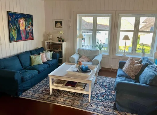 Sala de estar con asientos azules, una mesa de centro y ventanas grandes.
