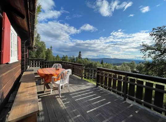 A wooden outdoor deck with seating overlooks a forested mountain landscape.
