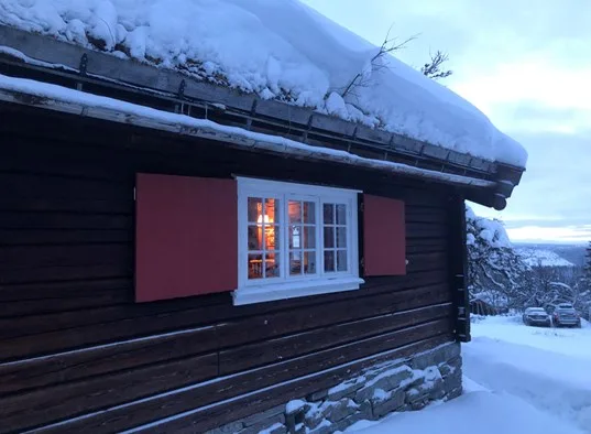 A snow-covered wooden building with a white-framed window and red shutters.