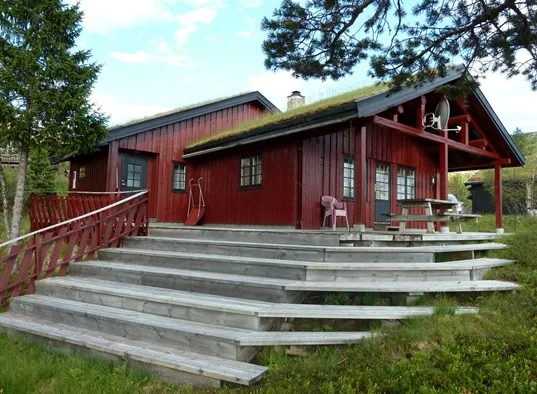 A red wooden cabin with a broad tiered deck and outdoor seating.