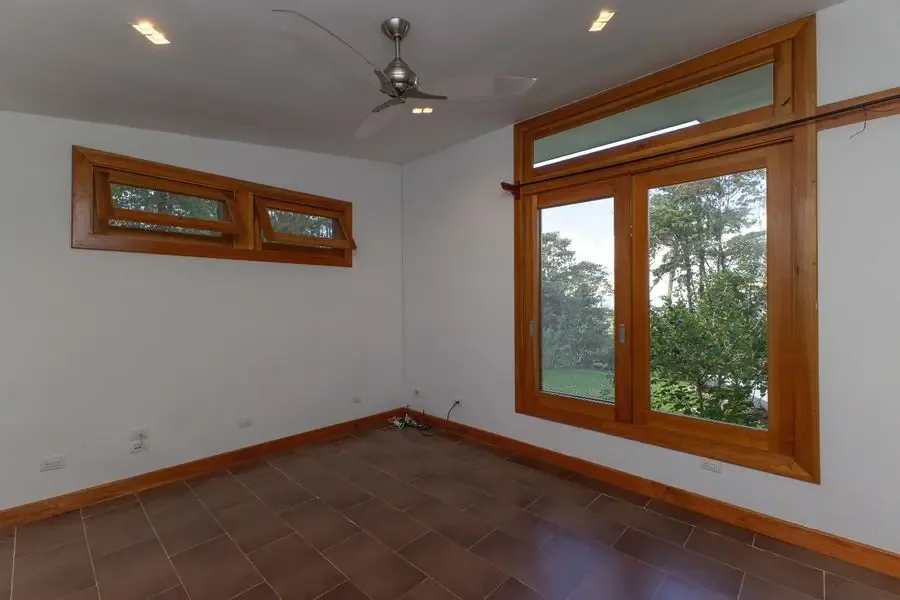 Una habitación vacía con grandes ventanas enmarcadas en madera y vista a la vegetación.