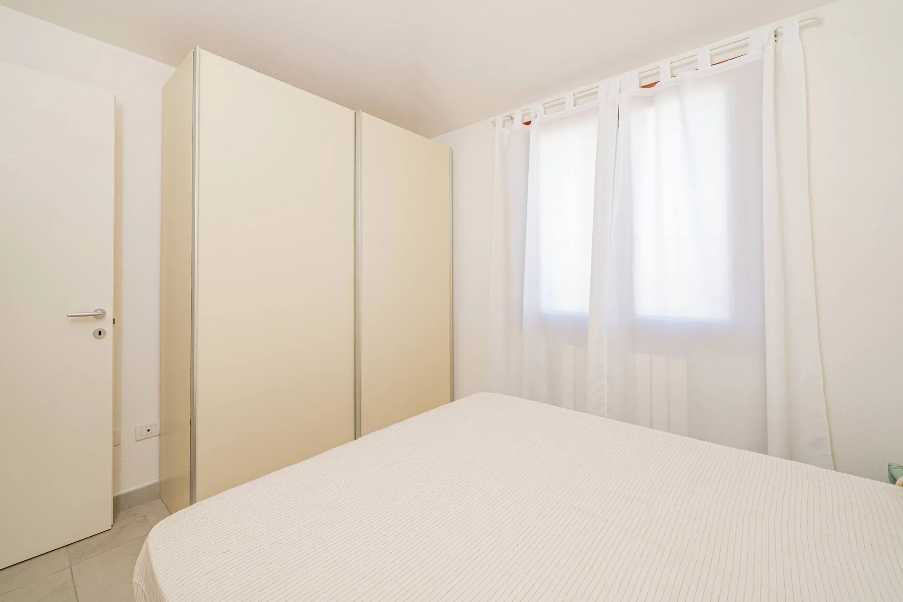 Un dormitorio luminoso con una cama, armarios empotrados y ventanas con cortinas.