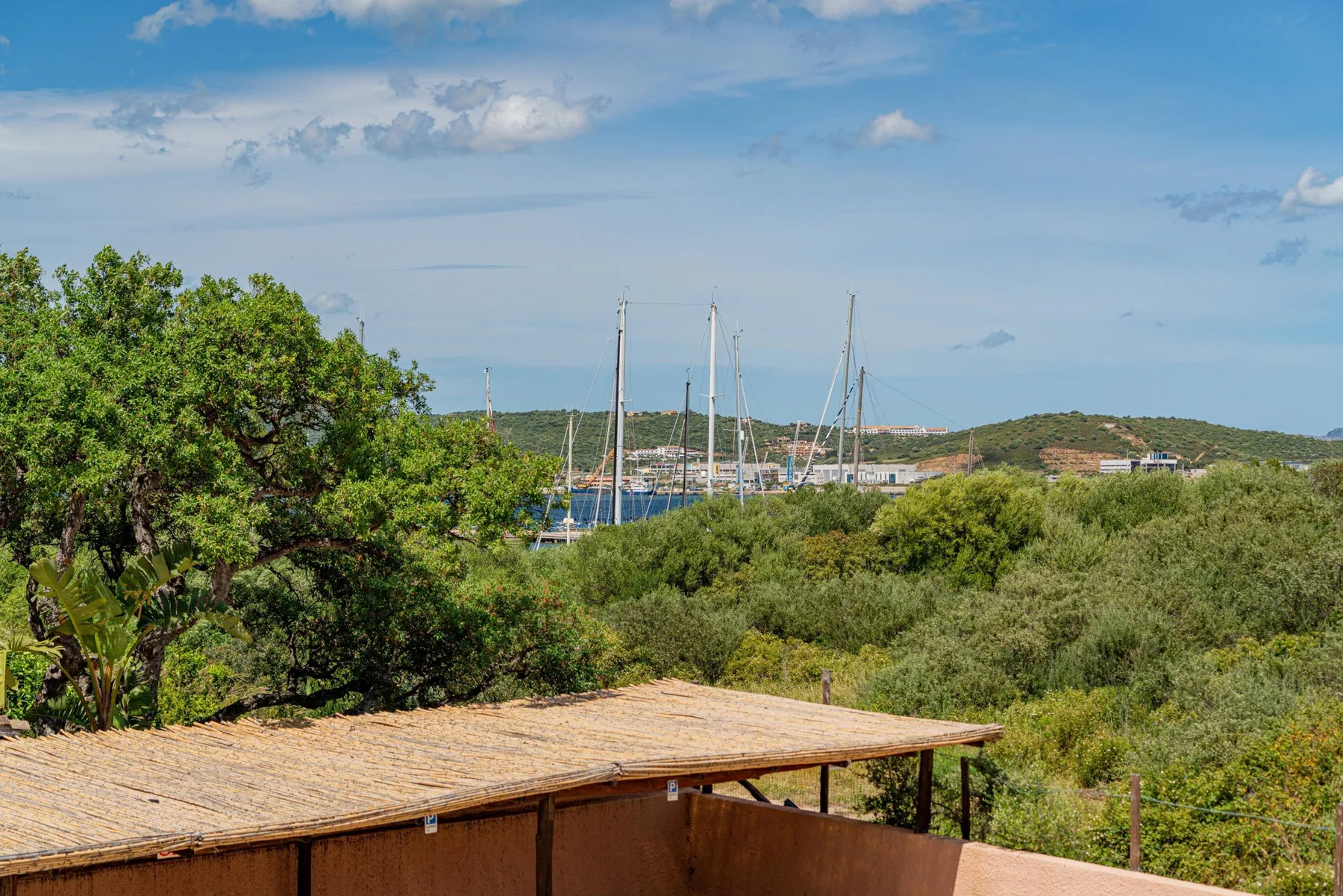 Una terraza de madera tiene vistas a colinas verdes y veleros en un puerto.