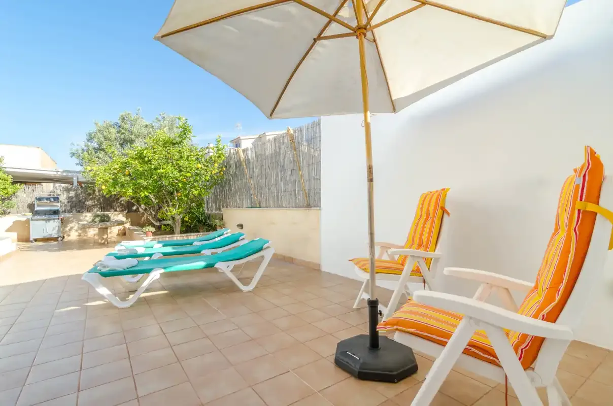 A sunny tiled patio has lounge seating, striped chairs, and a large umbrella.