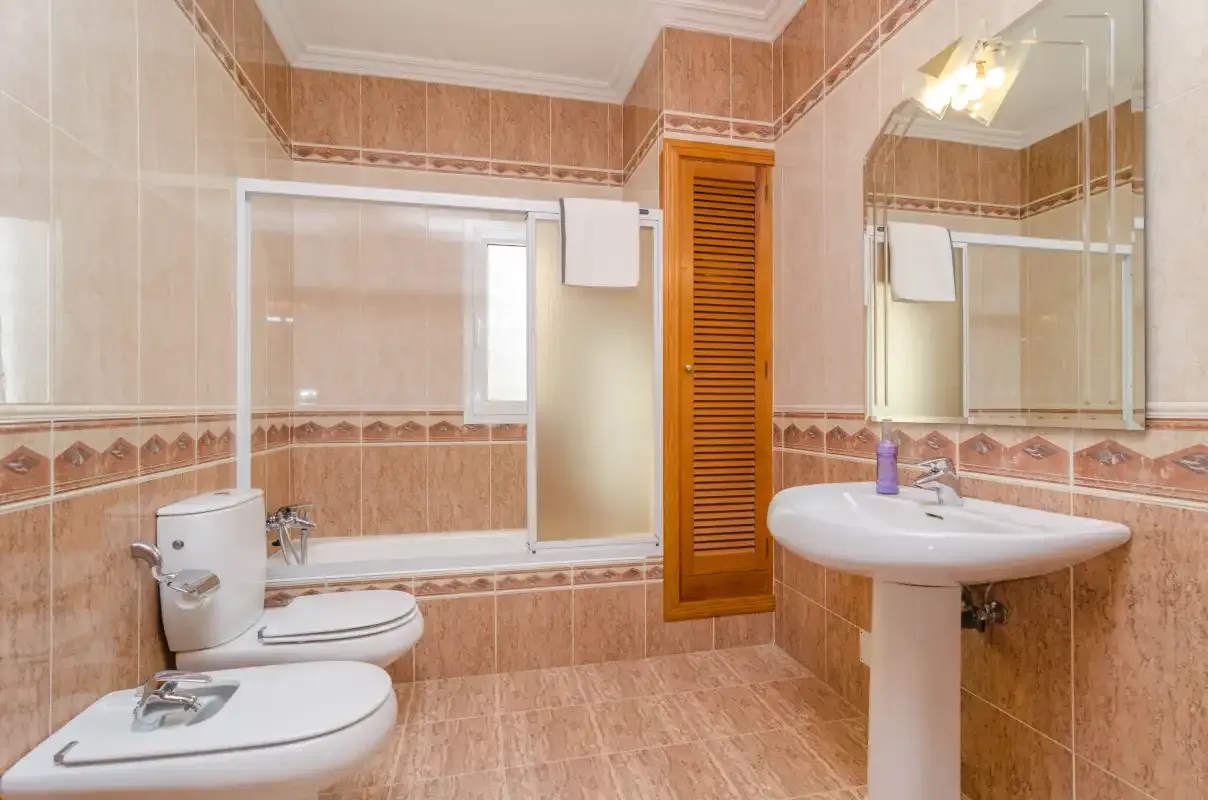 A tiled bathroom with a bathtub, toilet, and pedestal sink.