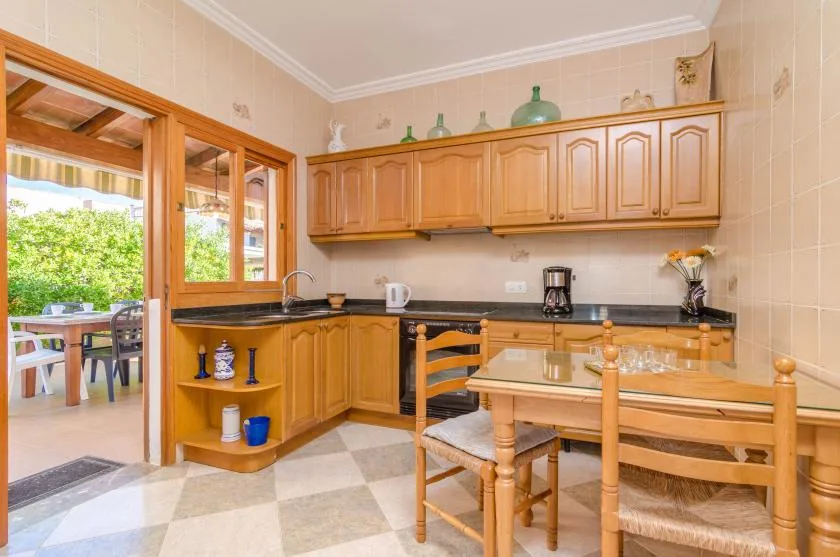 A tiled kitchen with wooden cabinetry, a dining table, and an open doorway to an outdoor seating area.