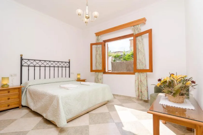 A bedroom with a bed beside an open window overlooking greenery.
