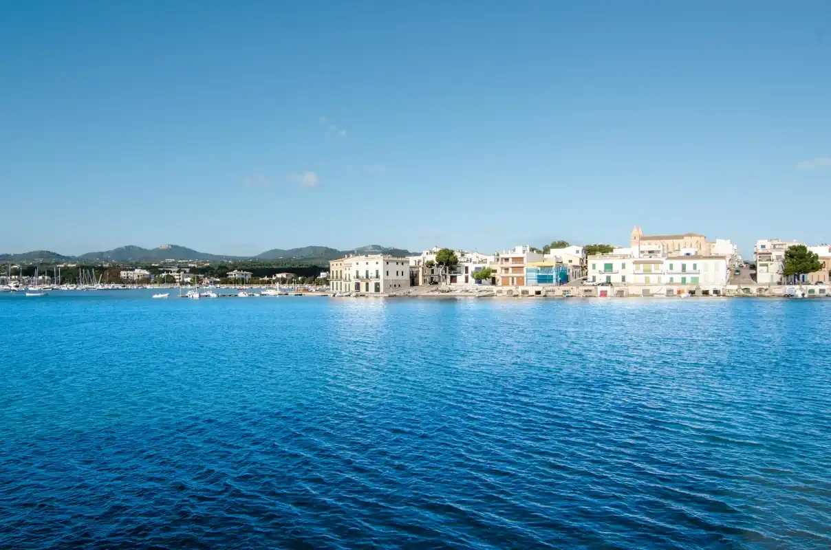 A coastal waterfront with buildings along the shore and blue water in the foreground.