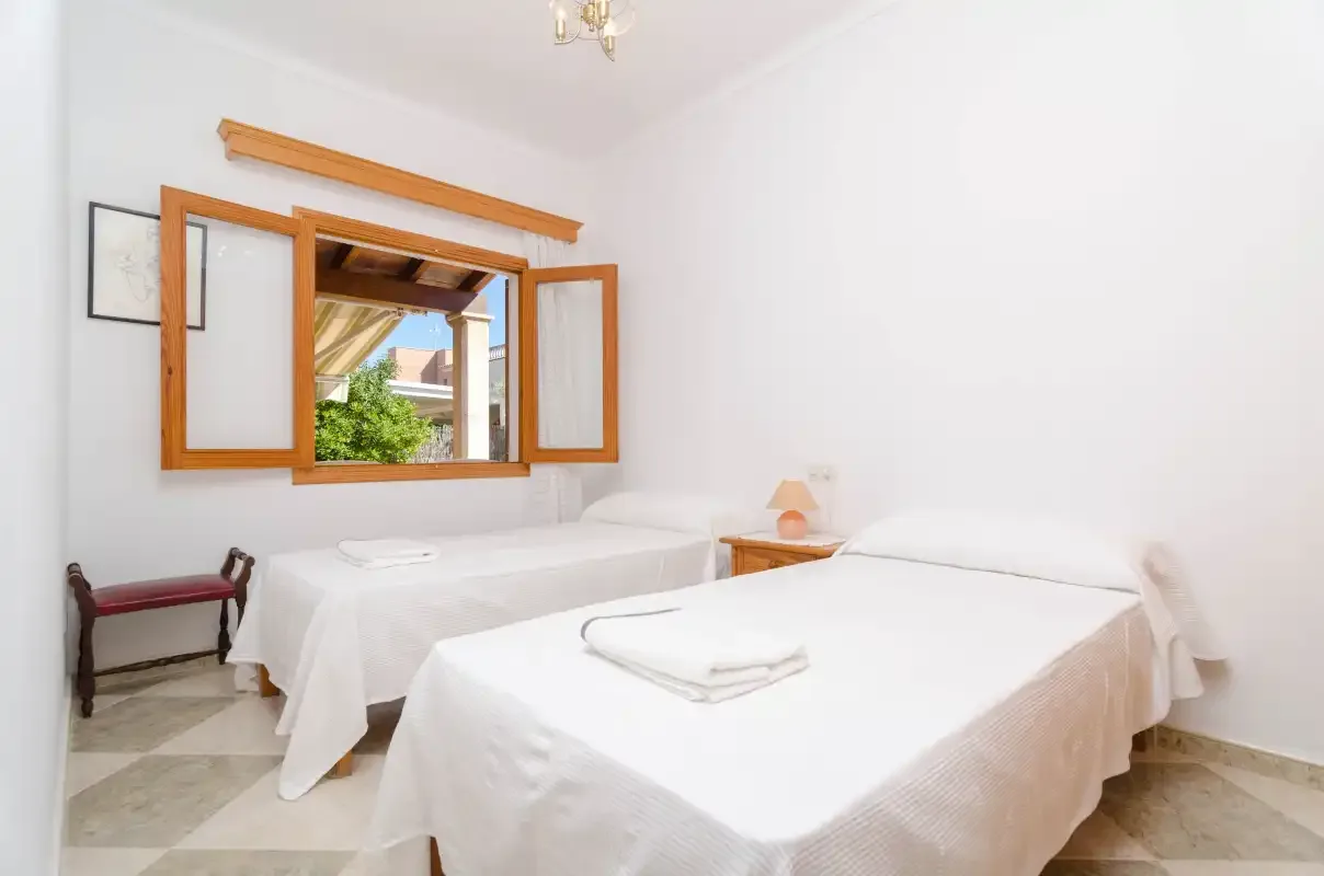 A bright bedroom with two beds and an open wooden window.