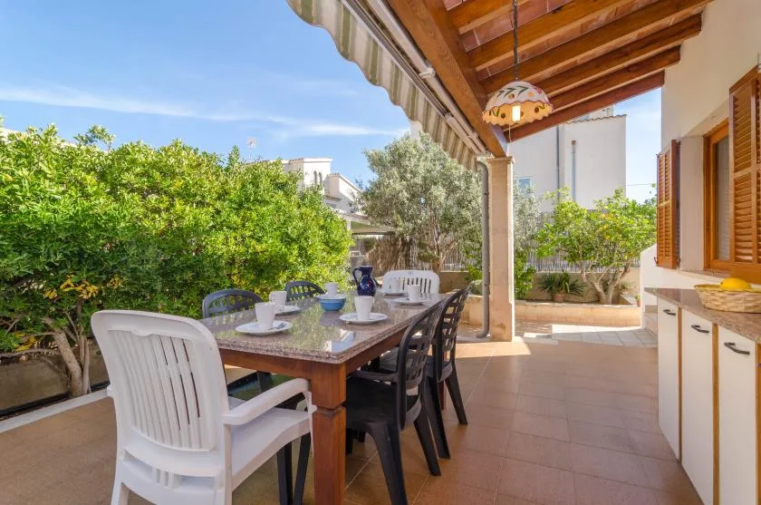 A covered outdoor dining area with a table and chairs beside a leafy garden.