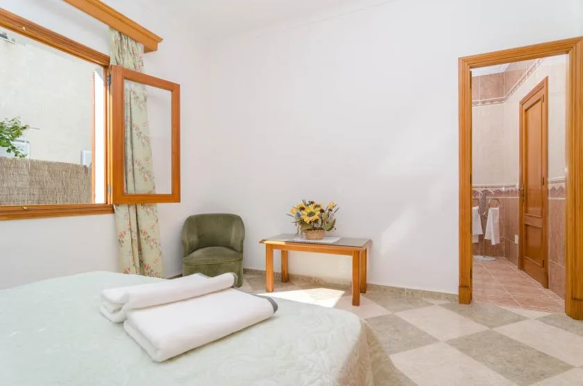 A bedroom with a bed, an armchair, and a small table beside the open bathroom doorway.