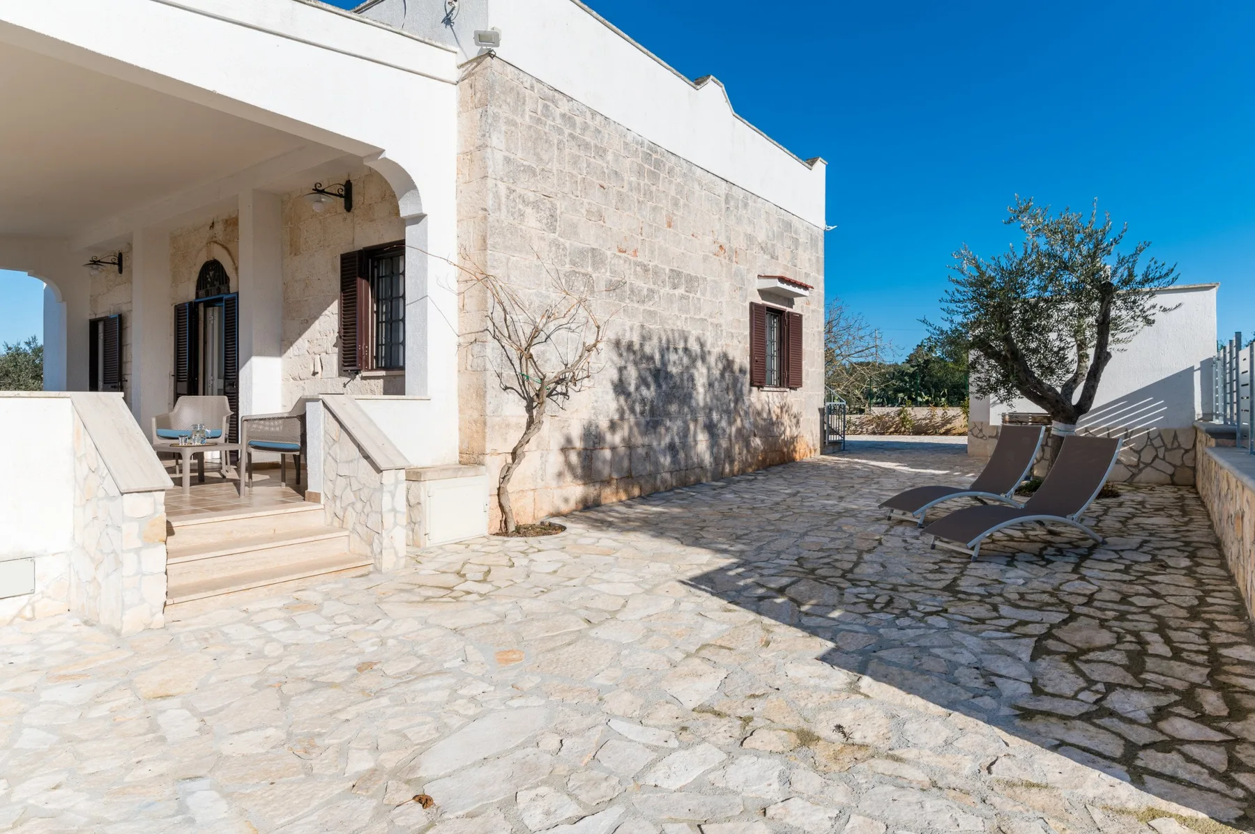A sunny stone patio with outdoor seating beside a light-colored building.