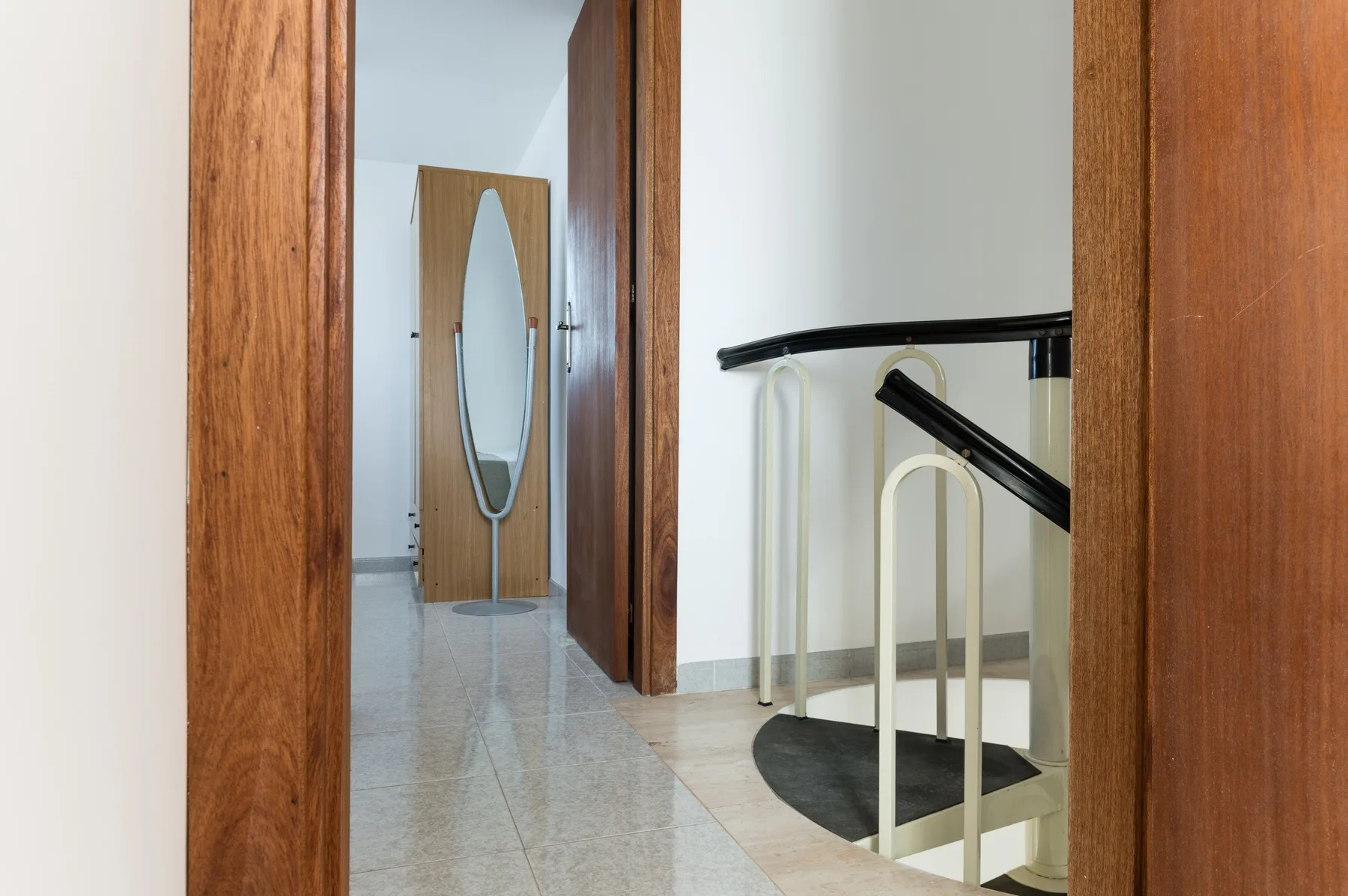 A tiled hallway leads past wooden doorways to a staircase with a dark handrail.