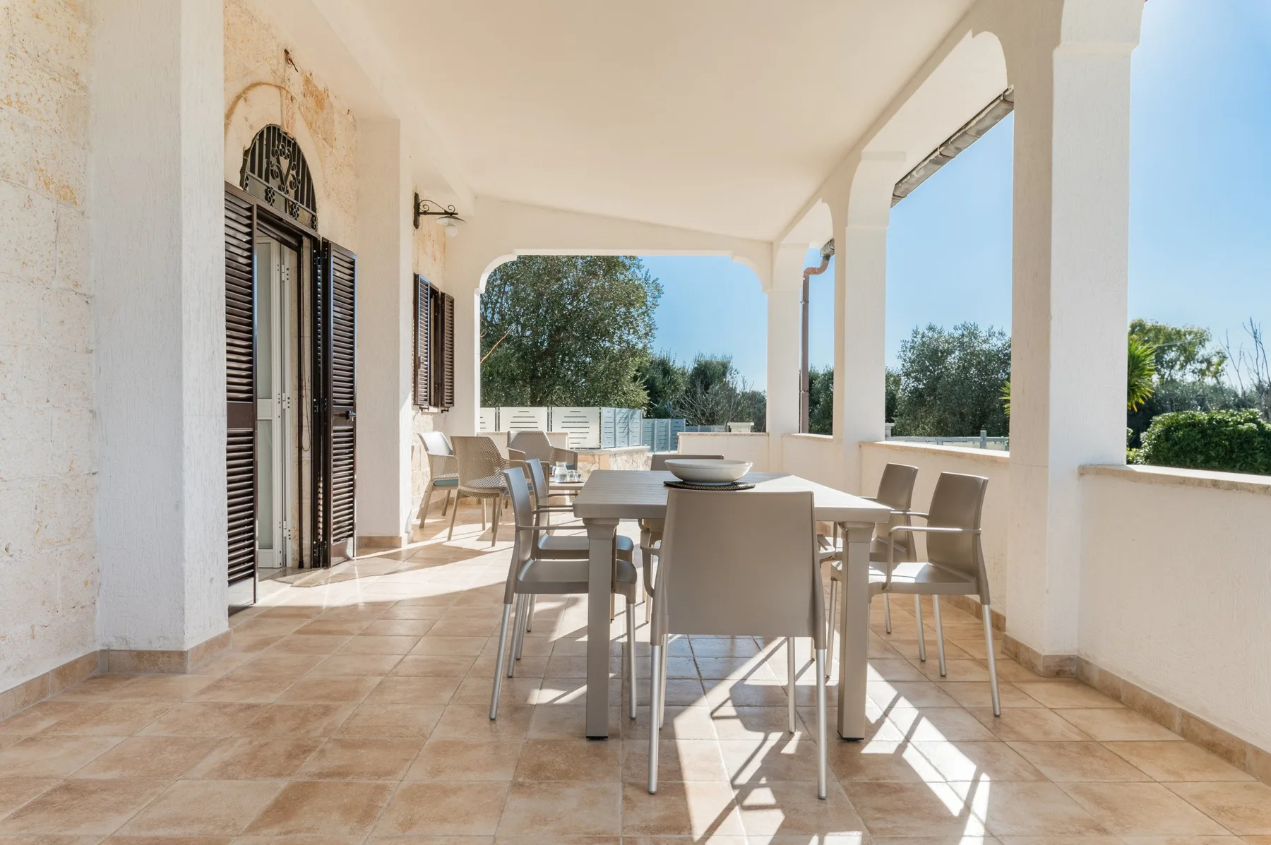 A covered outdoor dining area with a table and chairs overlooks greenery.