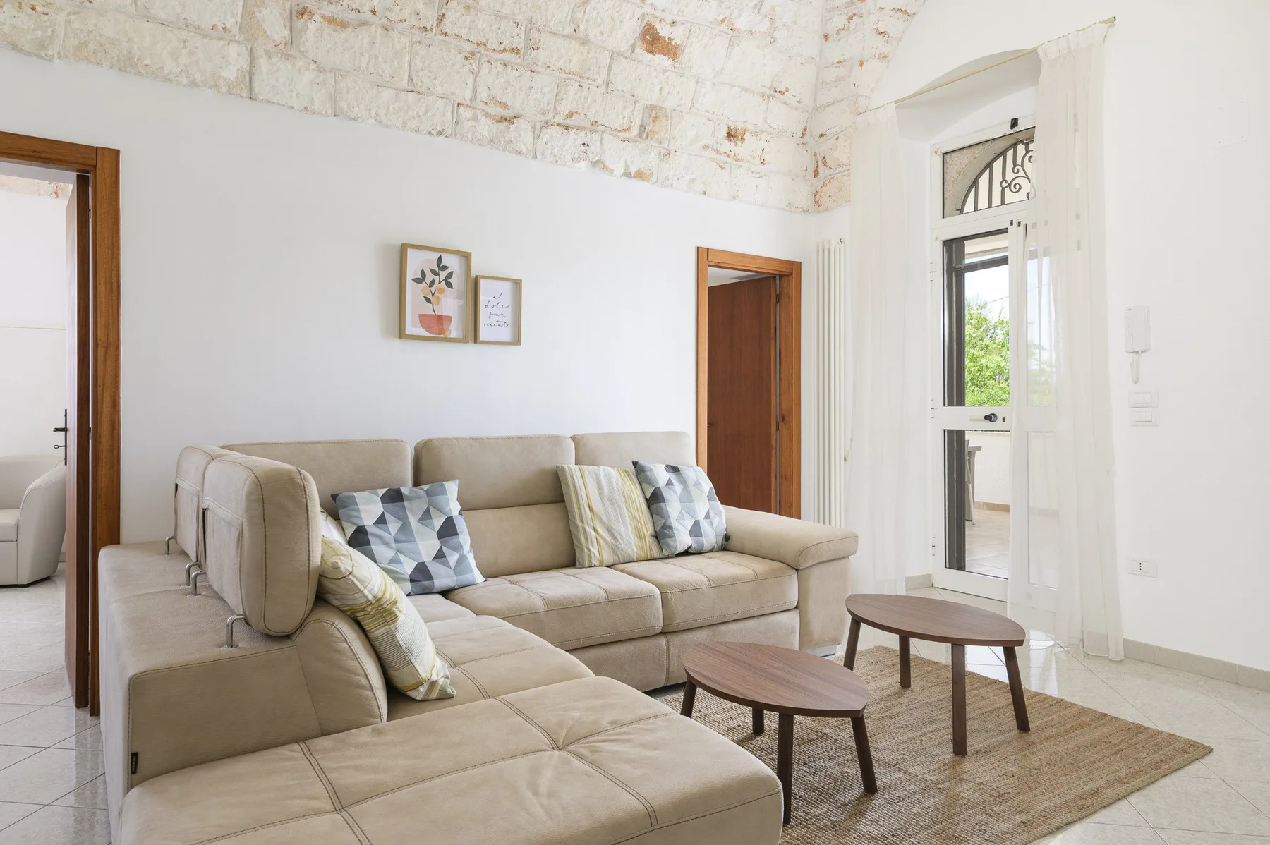 A bright living room with beige seating, two small tables, and a woven rug.