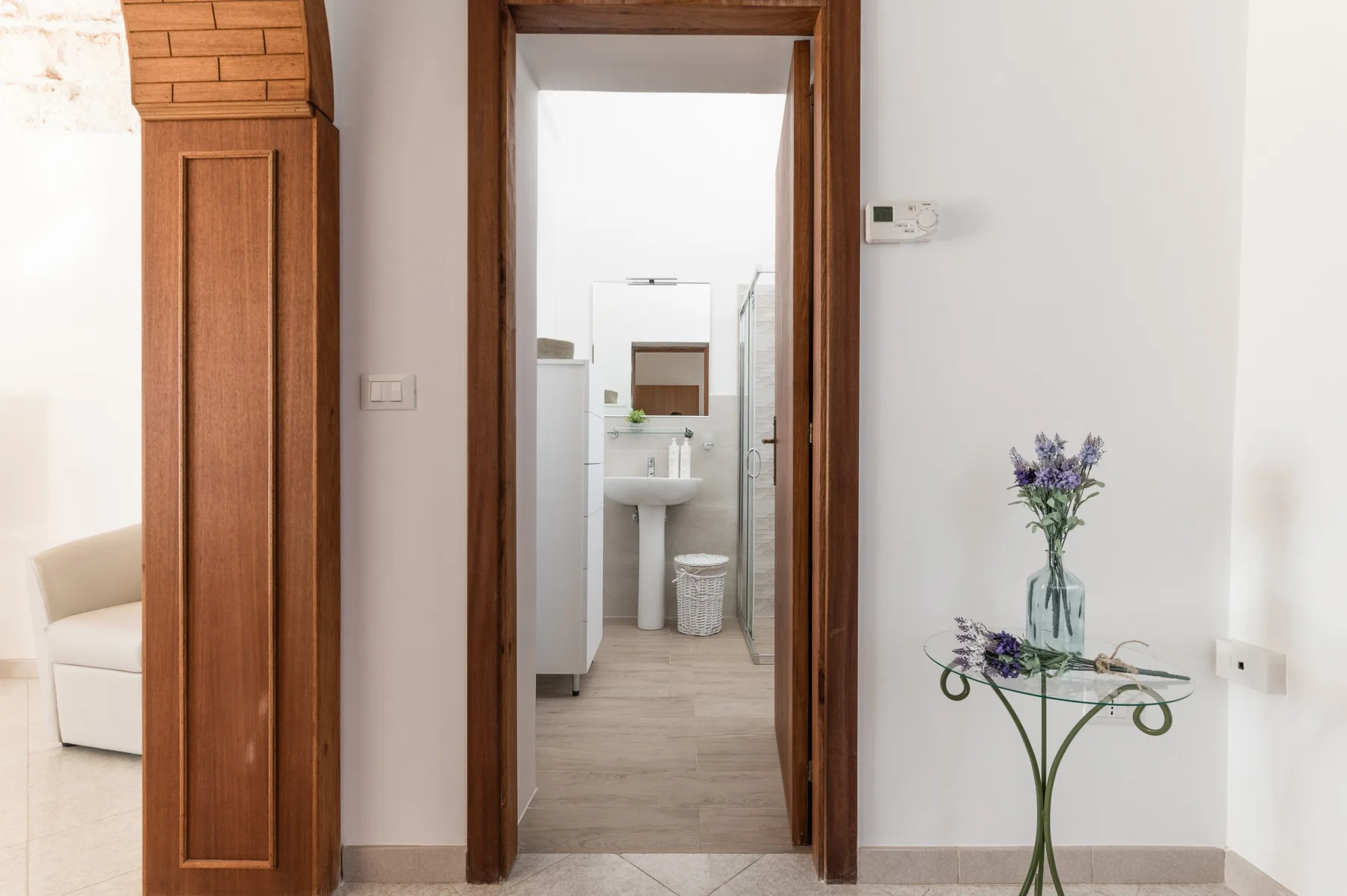 A bright interior hallway opens onto a bathroom, with flowers on a small glass table.