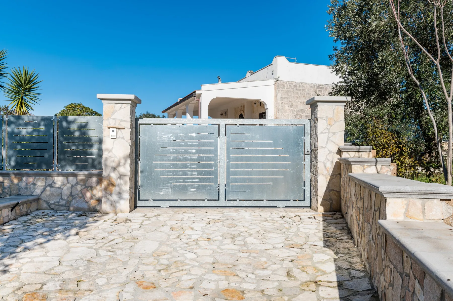 A stone-paved entrance leads to a pale building behind a metal gate.