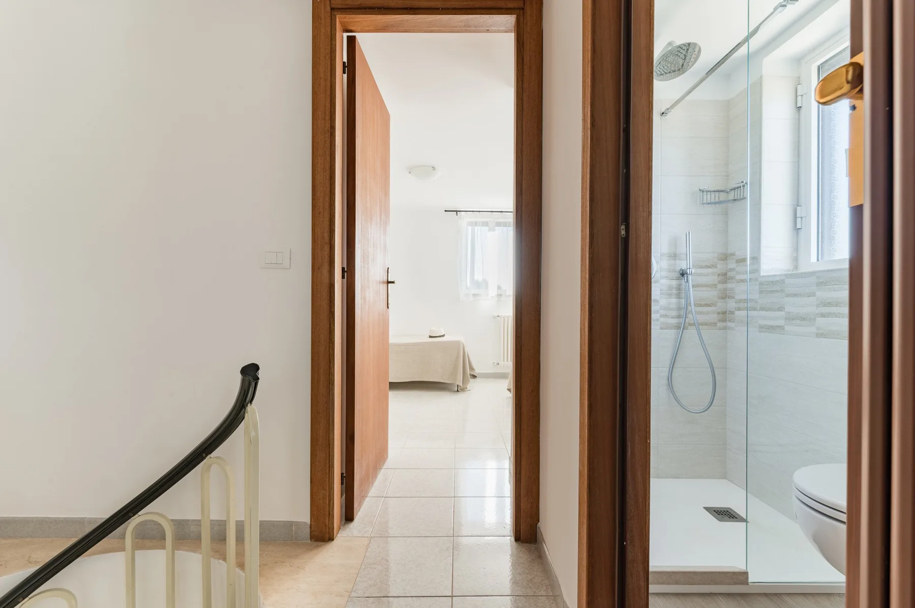 A hallway opens onto a bedroom and a bathroom with a glass shower.