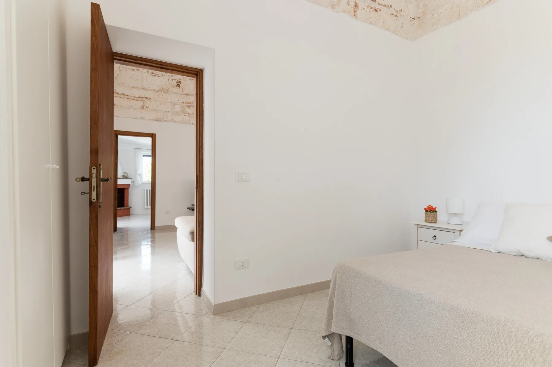 A bright bedroom with a bed beside an open wooden doorway.