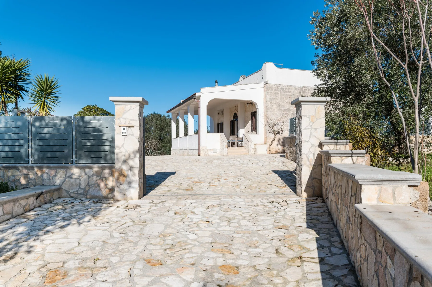 A stone-paved driveway leads to a white house with a covered porch.