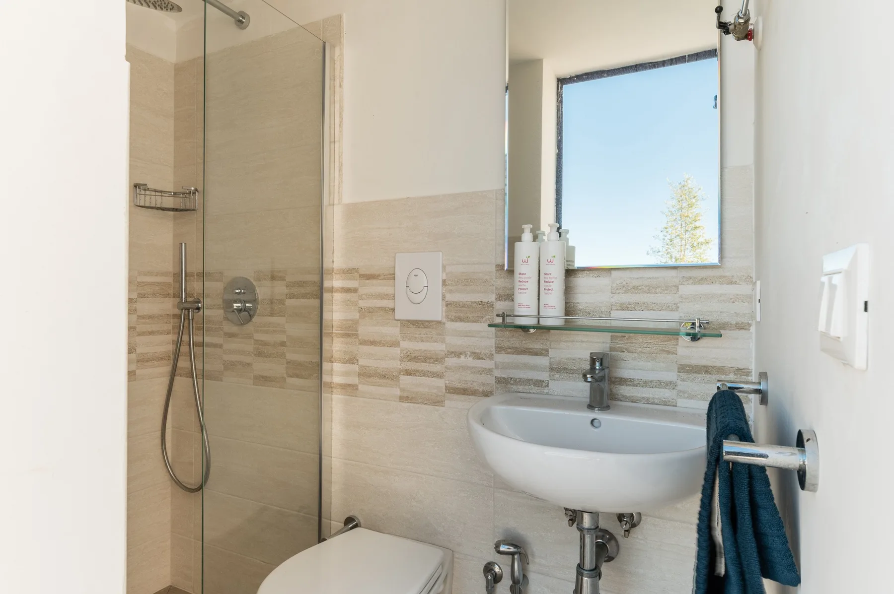 A tiled bathroom with a glass shower, sink, and window.