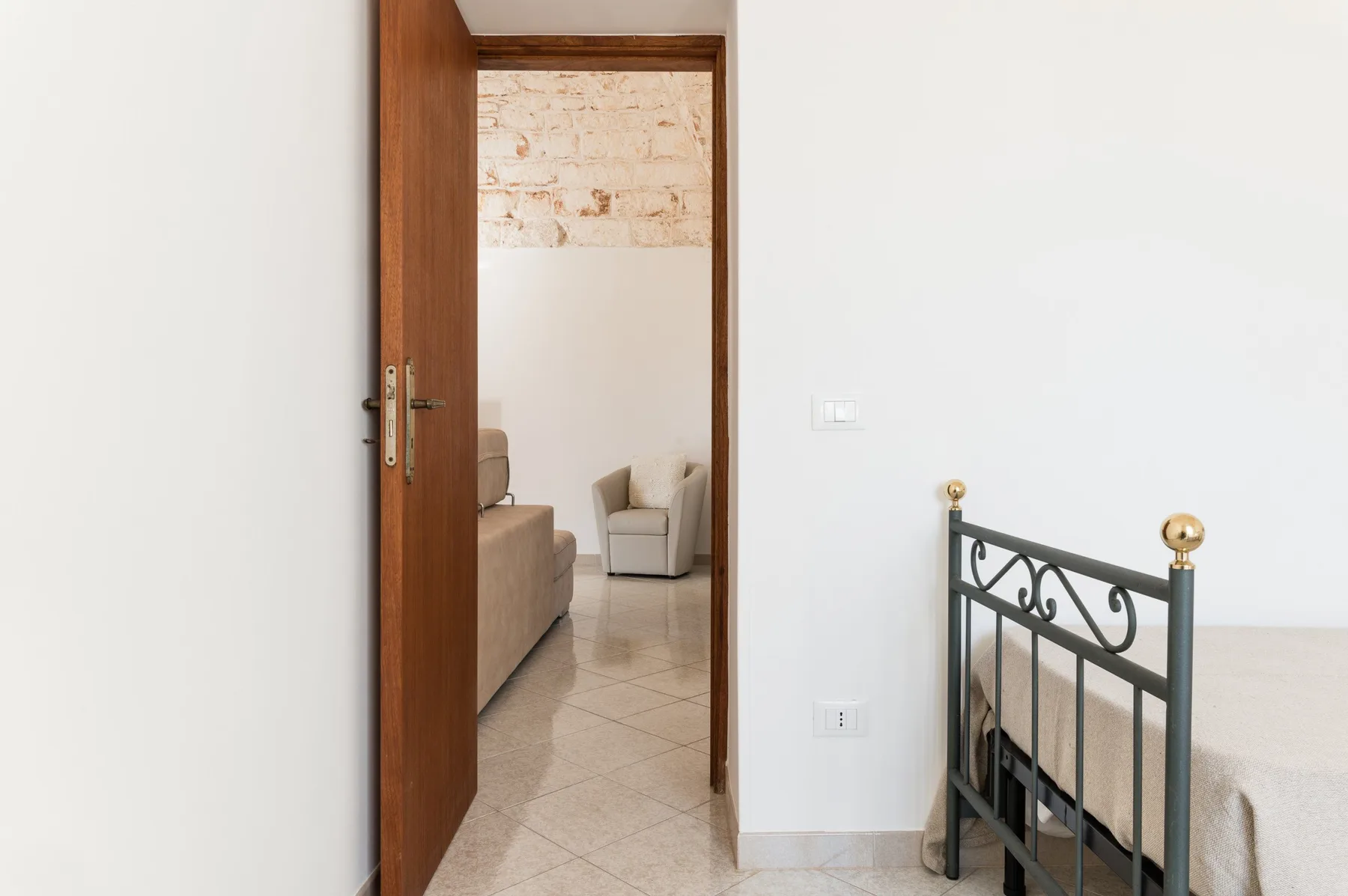 A bedroom doorway opens onto a sitting area, with a metal bed frame in the foreground.