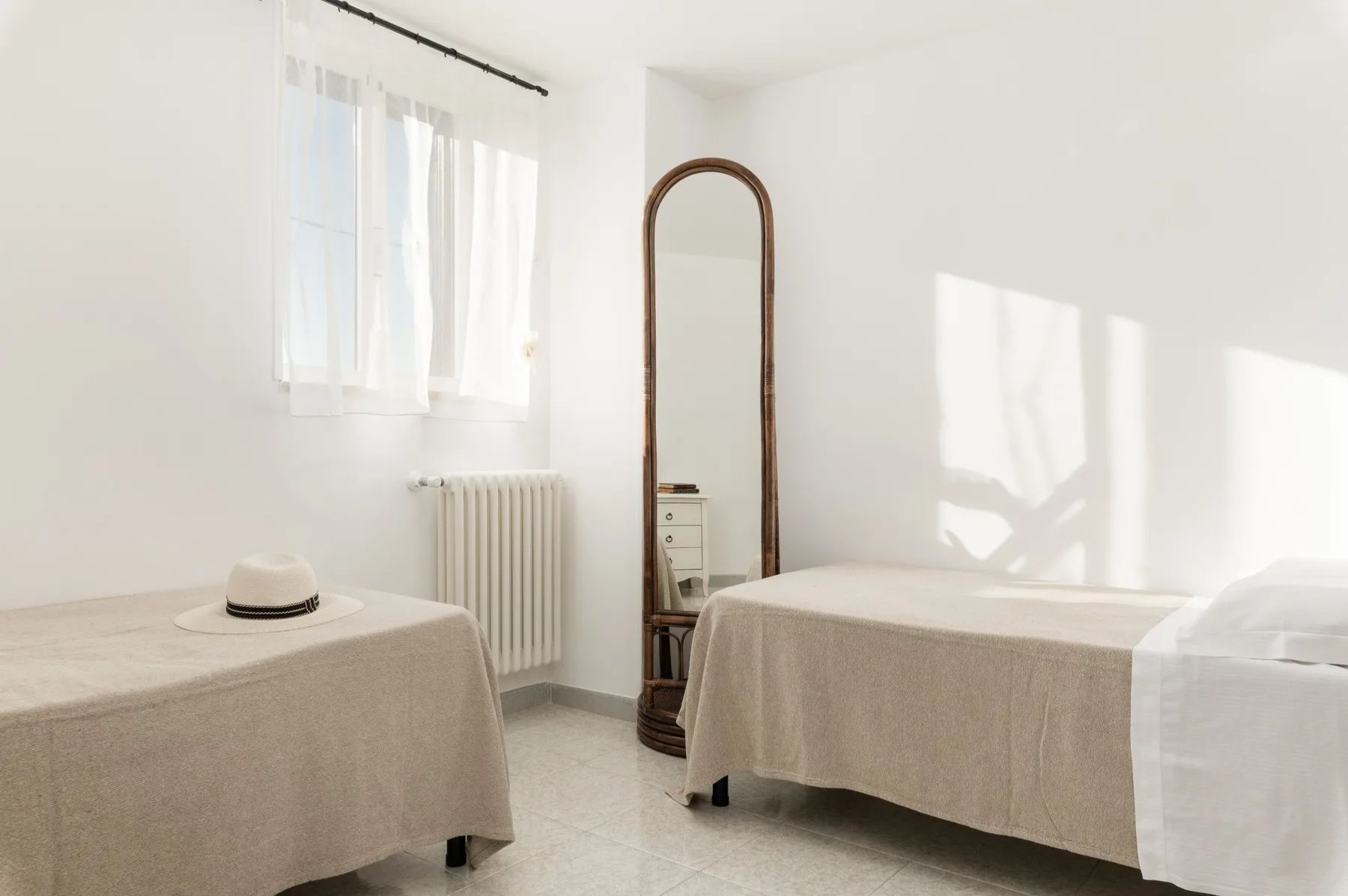 A bright bedroom with two beds and an arched standing mirror.