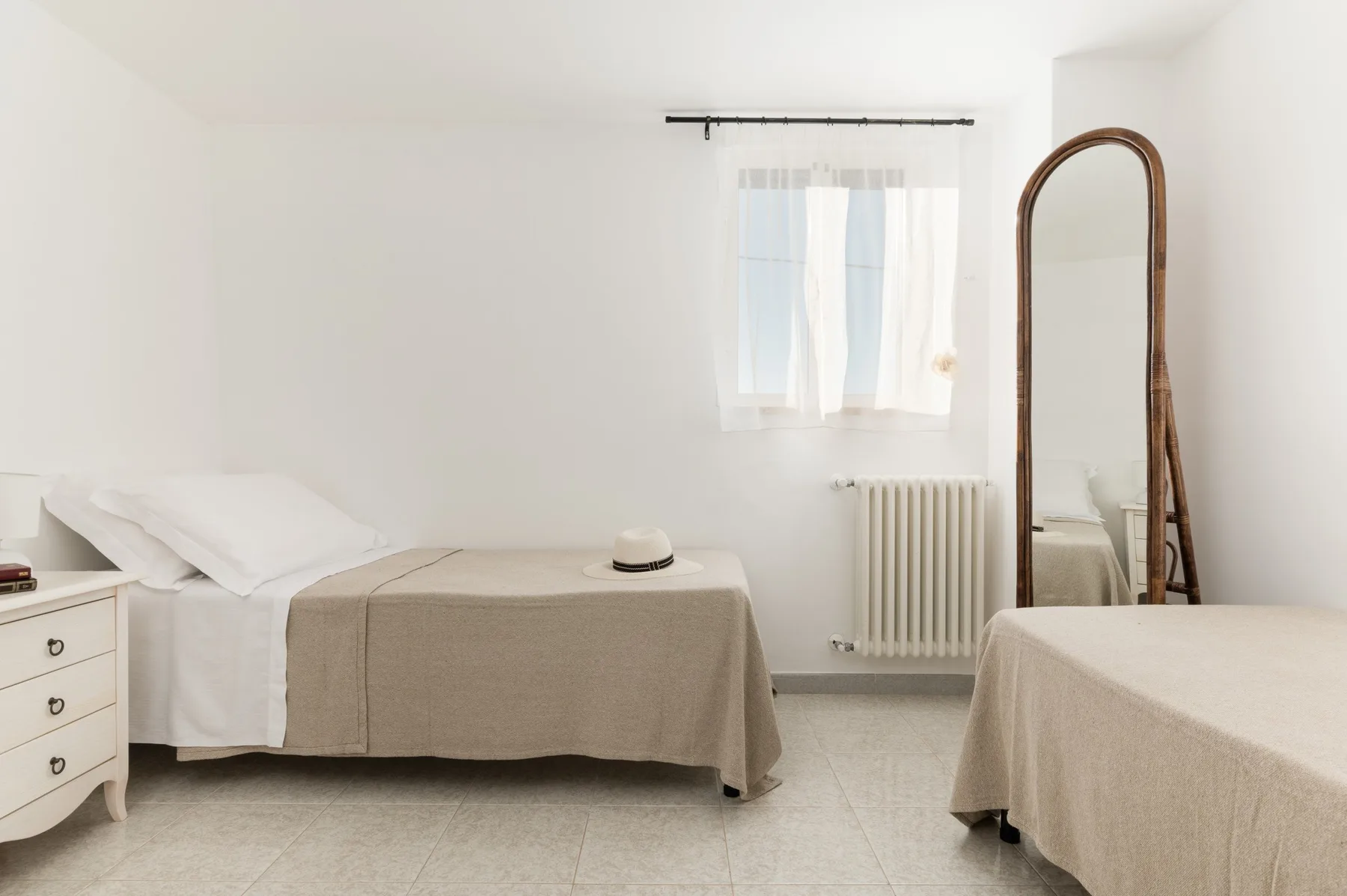 A bright bedroom with two beds and a window with sheer curtains.