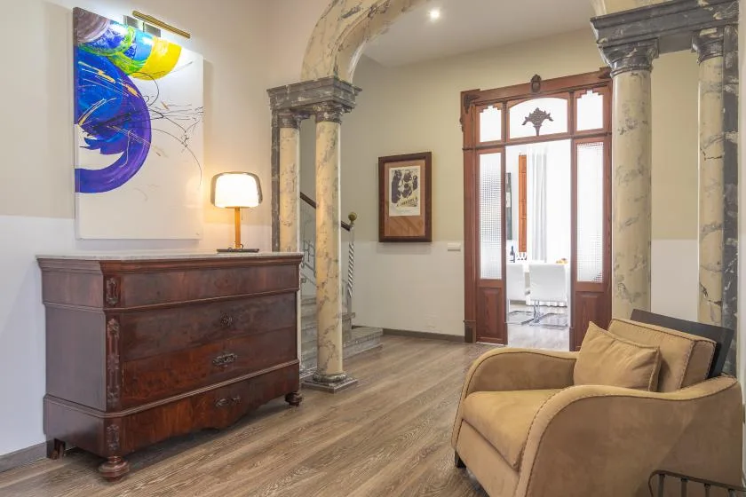 Sala de estar con un sofá color canela, una cómoda de madera y ventanas altas.
