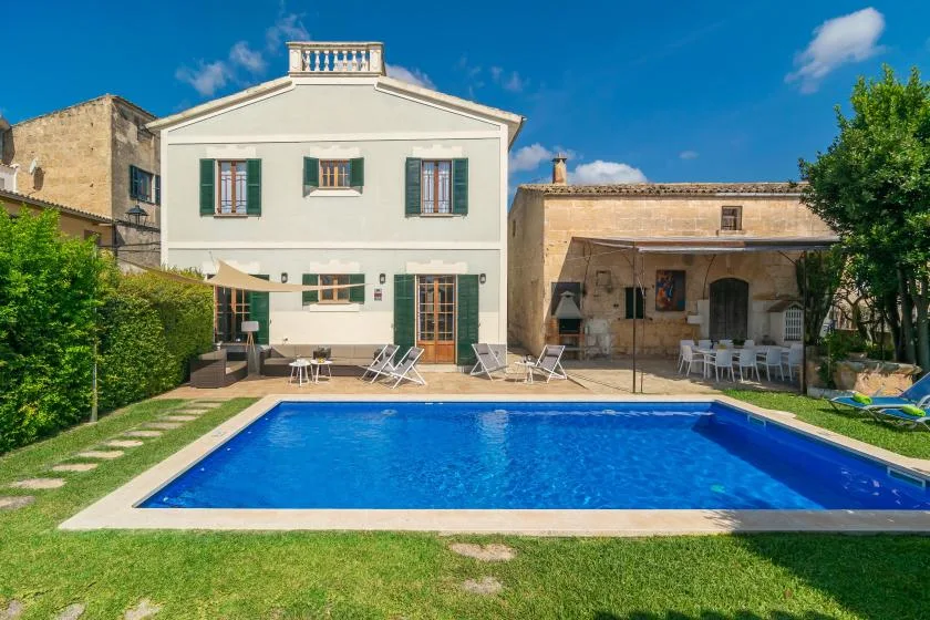 Una casa y un patio cubierto dan a una piscina y un césped.