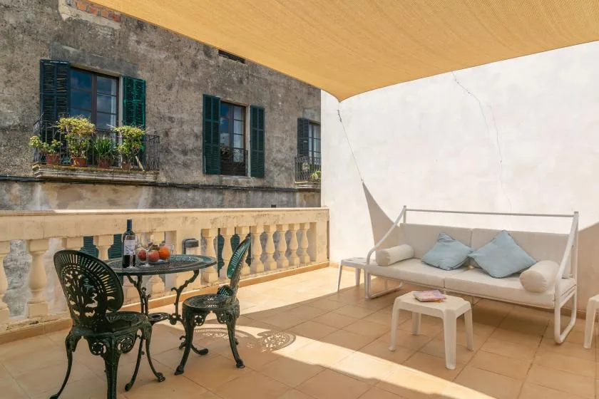 Una terraza soleada con una mesa y asientos junto a un edificio de piedra.